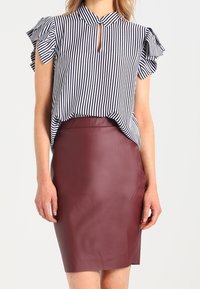 Randig blus med volang ärmar och nyckelhålsutringning; kombinerad med en figurnära bordeauxfärgad läderskjol. Söld väv, skräddarsydd design.