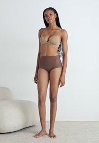 Sutien de culoare maro deschis cu bretele subțiri și design în formă de V, asortat cu chiloți maro cu talie înaltă. Textură de țesătură netedă, stil minimalist.