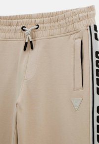 Beige sweatpants met een elastische tailleband, trekkoord, zijzakken en een logo-patch; heeft een zwart-witte merkzijde-streep.