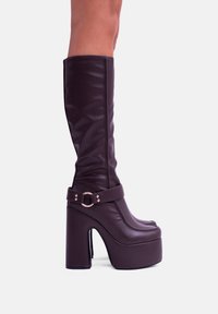 Stivali platform al ginocchio in finta pelle viola scuro, con un spesso tacco a blocco, punta arrotondata e una strap laterale con dettaglio in metallo a fibbia.