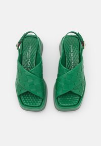 Zelené pletené kožené sandály s otevřenými prsty, křížovými řemínky, polstrovanou stélkou a mírným podpatkem. Detail s přezkou na zadní straně.