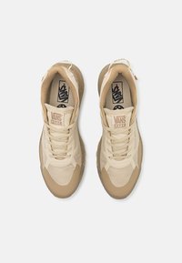 Kreminės spalvos Vans sportbačiai su sklandžiu ir tekstūruotu audiniu, apvaliu nosimi, raišteliais ir logotipu ant liežuvio. Padas turi dėmėtą apdailą.