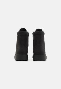 Botines negros con una textura suave y mate, presentan un puño plegado, cremalleras laterales y una suela de goma resistente para mayor tracción.