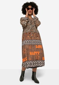 Robe à imprimé léopard marron avec taille élastique, motifs de texte orange, motifs d'étoiles et détails noirs ; associée à des bottines noires à clous.