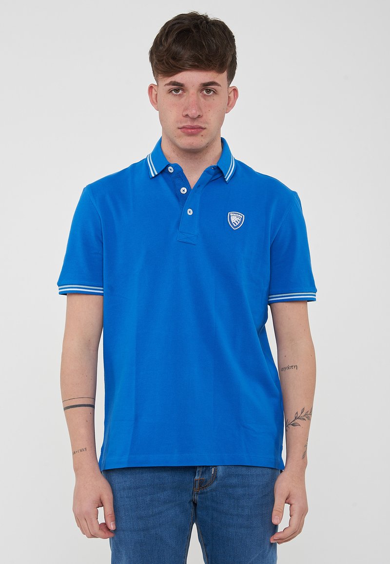 Polo shirt blu royal in cotone con colletto a righe bianche e patta con tre bottoni, logo ricamato sul lato sinistro del petto. Maniche corte.