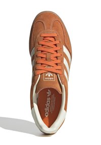 Brune ruskinds sneakers med hvide striber og snørebånd. Med en orange inderside og et logo på tungen. Klassisk design med lav profil.