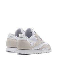Valge ja beeži värvi Reebok'i tennisekingade paar, nurga alt, et näidata selja- ja külgpinda, nahast aktsentide ning logoga kandmisel ja küljes.