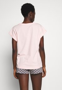 Lichtroze katoenen t-shirt met korte mouwen, ronde halslijn en een relaxte pasvorm, gecombineerd met gestreepte zwart-witte shorts.