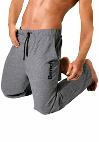 Graue Sporthosen aus einem weichen, strukturierten Stoff mit einem Kordelzugbund. Mit einem schwarzen Logo am linken Bein. Lässiger, lockerer Schnitt.