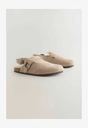 Bežiniai zomšos klumpiai su reguliuojamu užsegimu, atviru kulnu, tekstūruota paviršiumi ir lengvu guminio padu.