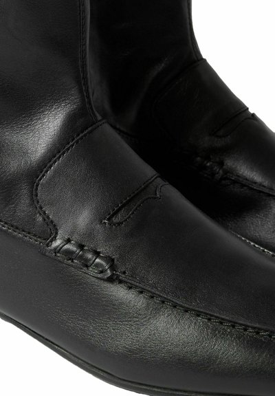 Zapatos de cuero negro con un acabado suave, que presentan costuras decorativas y un diseño estilo mocasín. Punta redondeada y suela flexible.