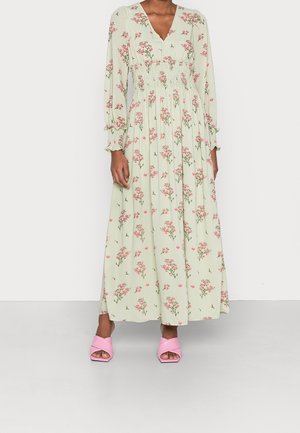 Dlouhé mintově zelené šaty s květinovým vzorem, s výstřihem do V, nařaseným pasem a dlouhými rukávy. Doplněné růžovými sandály s masivním podpatkem.