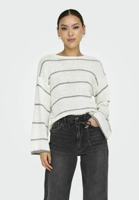 Pull en tricot blanc avec des rayures grises, à manches longues et encolure bateau, associé à un jean en denim noir taille haute.