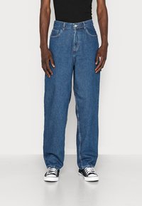 Siniset farkut, joissa on löysä istuvuus, viisi taskua, nappikiinnitys, erottuvat ompeleet ja suora lahjetyyli.