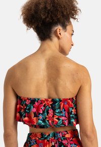Blumiger Crop-Top mit Rüschensaum, der leuchtend rote, pinke und blaue Blumen auf schwarzem Hintergrund zeigt. Weicher Stoff mit elastischen Bändern.