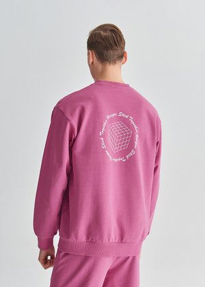 Różowy sweatshirt wykonany z miękkiego materiału, z graficznym wzorem sześcianu i napisem na plecach, z prążkowanymi mankietami i dołem.