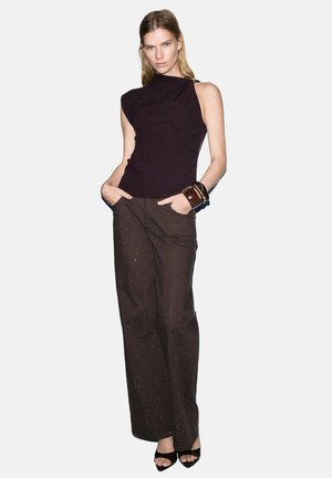 Haut sans manches noir avec un col asymétrique, associé à un pantalon à rayures fines marron avec un léger éclat et une coupe évasée.