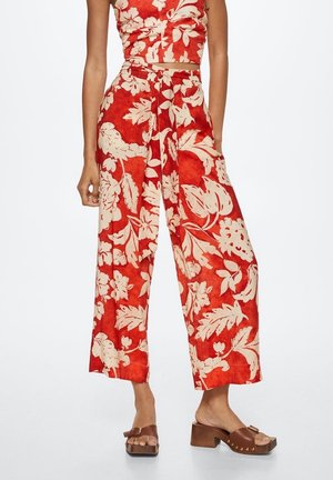 Woman wearing high-waist wide-leg red pants with large beige floral print, paired with brown open-toe block heel sandals.