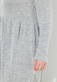 Robe grise à manches longues en tissu tricot doux, avec une taille froncée et une texture plissée, ainsi que des poignets ajustés.