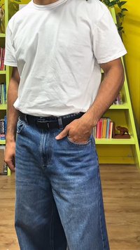 Bílé bavlněné tričko nošené s světle modrými džínami. Džíny mají volný střih a jsou upevněny černým páskem. Pozadí tvoří dřevěná podlaha.