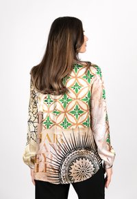 Seidenhemd mit filigranen Mustern in Grün, Gold und Beige, mit floralen und geometrischen Designs. Lange Ärmel und lockere Passform.