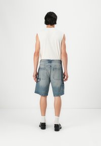 Shorts in denim azzurro chiaro con effetto sbiadito, dotati di più tasche e una vita standard, abbinati a un top senza maniche bianco.