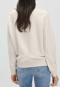 Sudadera de color beige claro con cuello redondo y mangas raglán. Terminada con puños y dobladillo acanalados. Combinada con vaqueros azules.