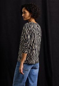 Langsleeve top met een beige en zwarte zebra-print, met een ronde halslijn. Gecombineerd met losse blauwe jeans, gezien vanaf de zijkant.