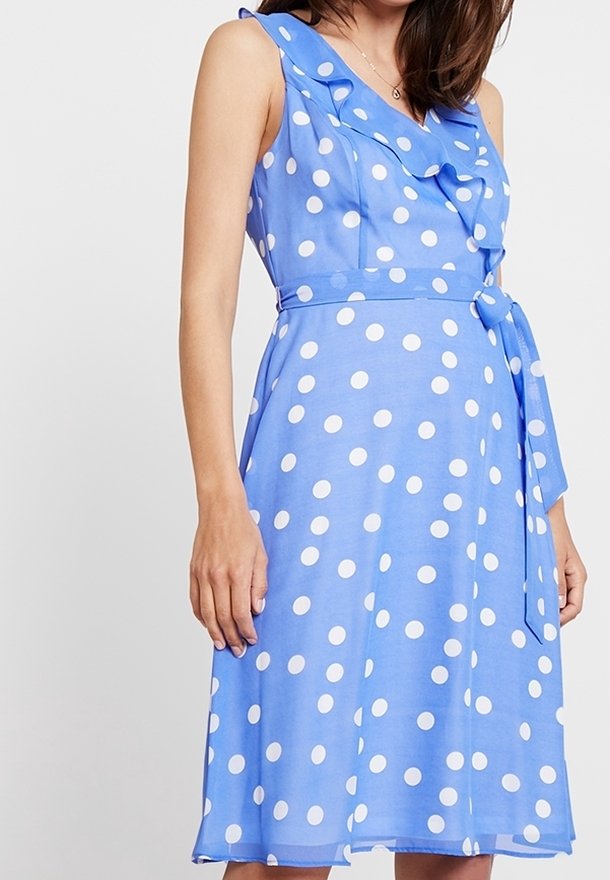 Robe bleu à pois avec un col froncé, sans manches, taille ceinturée et jupe à mi-genoux en tissu léger.