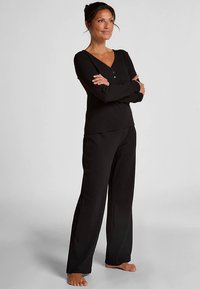 Zwart top met lange mouwen en knoopsluiting, gecombineerd met bijpassende broek met wijde pijpen, gemaakt van een zachte stof die geschikt is voor loungewear.