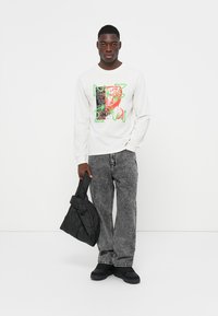 Hvit langermet skjorte med abstrakt flerfarget grafisk design. Kombinert med svarte teksturerte jeans og en svart veske. Svarte sko.