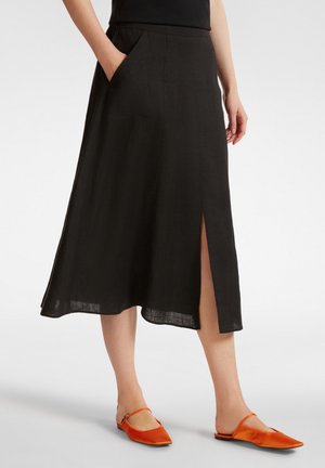 Gonna midi nera in lino con tasche laterali, caratterizzata da uno spacco anteriore, abbinata a scarpe arancioni slip-on. Tessuto morbido e drappeggio delicato.