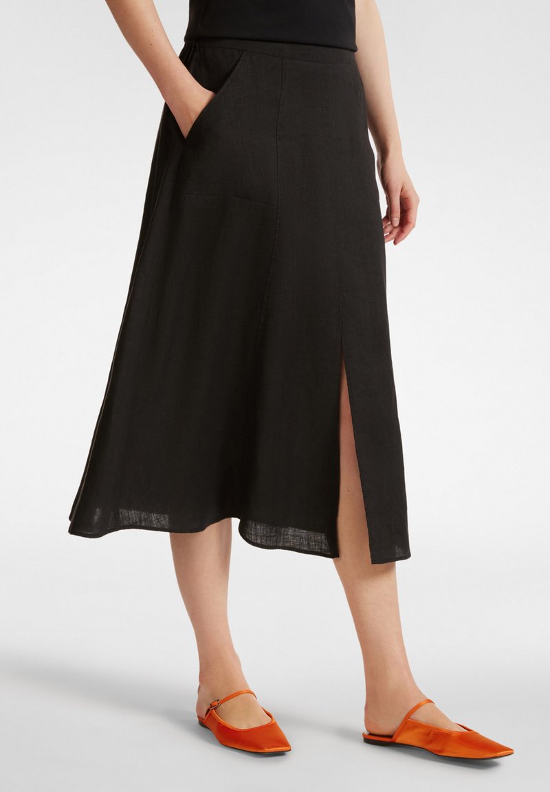 Gonna midi nera in lino con tasche laterali, caratterizzata da uno spacco anteriore, abbinata a scarpe arancioni slip-on. Tessuto morbido e drappeggio delicato.