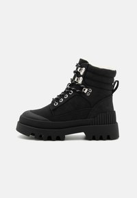 Bottines noires à chevilles avec un dessus rembourré, des accents texturés, un matériel métallique, des lacets, et une semelle en caoutchouc épaisse présentant un motif dentelé.