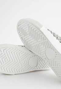 Sneakers bianchi con una suola in gomma testurizzata, motivo geometrico sulla parte superiore e una punta liscia. Il design presenta fori di ventilazione.