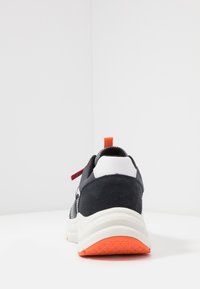 Sportliche Sneakers mit einem dunkelblauen Wildleder-Obermaterial, weißen und orangefarbenen Akzenten, strukturiertem Sohle und einer Zuglasche an der Ferse für einfaches An- und Ausziehen.