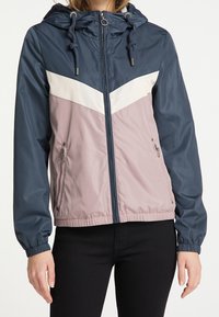 Giacca leggera con cappuccio in blu navy, bianco e malva. Presenta una chiusura zip frontale, polsi elasticizzati e due tasche laterali. Tessuto liscio e resistente all'acqua.