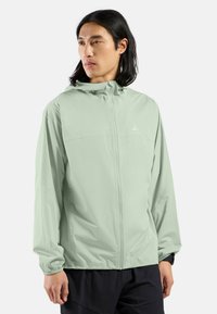 Light green lightweight jacket with a hood, full zipper, and elastic cuffs. Made from smooth fabric, features a logo on the chest.