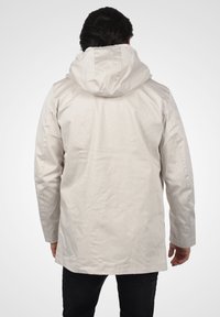 Lys grå vanntett jakke med hette, med rett snitt og glatt overflate, vist fra baksiden.