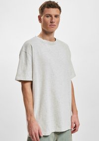 Lys grå oversized t-skjorte laget av myk stoff, med rund hals, korte ermer og en avslappet passform.