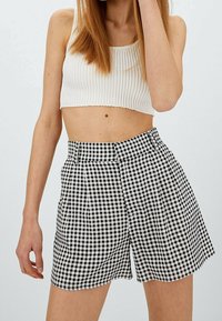 Top corto de canalé blanco combinado con pantalones cortos de tiro alto en un patrón de cuadros en blanco y negro, con pliegues y un dobladillo festoneado.