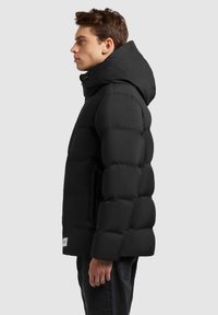 Chaqueta acolchada negra con un alto cuello, capucha y secciones rectangularmente acolchadas. Presenta un cierre frontal con cremallera y bolsillos laterales.