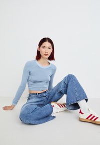 Light blue long-sleeve cropped top with ribbed texture, paired with loose denim jeans. White sneakers with red stripes and white ankle socks.