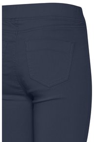 Posnetek v bližini temno modrih prilagojenih hlač, ki prikazujejo zadnji žep in detajle šivov na pasu.