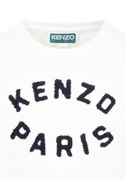 T-shirt blanc à manches courtes avec du texte duveteux bleu marine écrivant "KENZO PARIS" disposé en motif circulaire. Étiquette : KENZO KIDS.
