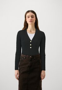 Cardigan noir à côtes avec un col en V, doté de trois boutons dorés et de manches longues, associé à une jupe en denim brun foncé.