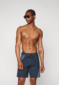 Dark blue swim trunks with a drawstring waist, featuring black and gray checkered side panels and a smooth, lightweight fabric texture.