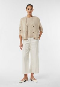 Jasnobeżowy kardigan z guzikami, w połączeniu z beżową dzianinową bluzką i kremowymi spodniami o szerokich nogawkach. Stylizacja wyróżnia się gładkimi fakturami i luźnym krojem.