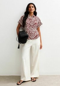 Blusa corta de manga corta con patrón rojo y blanco, con cuello, combinada con pantalones anchos blancos y bolso de mano tejido negro con sandalias.