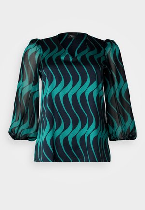 Mørk marineblå bluse med teal bølgemønster, V-hals, og gjennomsiktige puff-sleeves. Glatt stoff med en lett avslappet passform.